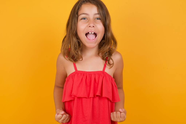 schöne kleine Mädchen in rotem Kleid schreit auf gelbem Hintergrund  - Foto, Bild