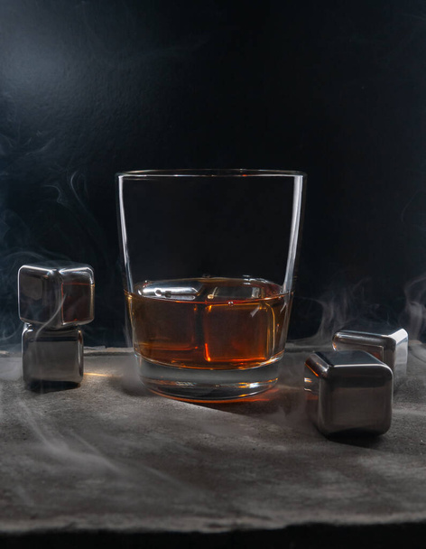 Steel cubes imitating ice. For cooling drinks. With a glass of whiskey. On a dark background. - Фото, зображення