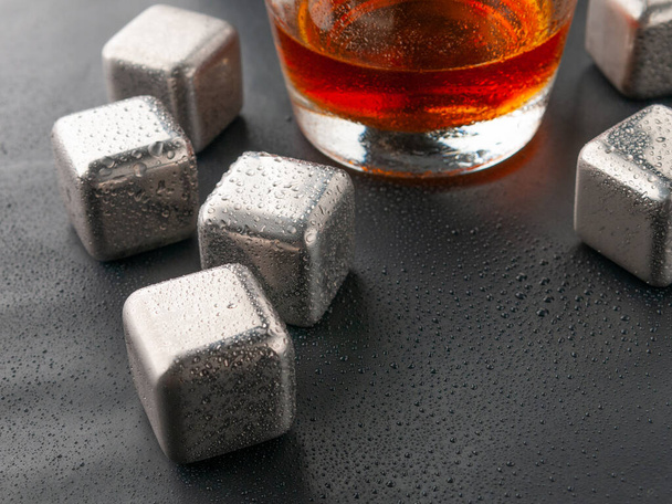 Steel cubes imitating ice. For cooling drinks. With a glass of whiskey. Covered with drops. Close-up. - Фото, изображение