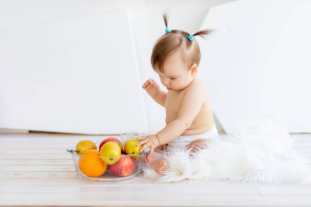 Parlak bir odada elinde meyve tabağıyla oturan küçük bir kız. - Fotoğraf, Görsel