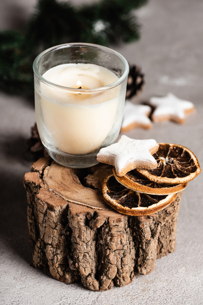 Selective focus of candle with dried orange slices and cookie on wooden stand - Valokuva, kuva