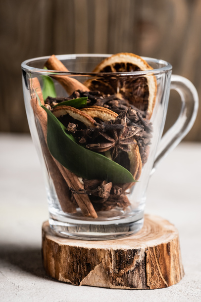 Selective focus of glass cup with spices and orange dried slices on wooden stand - 写真・画像