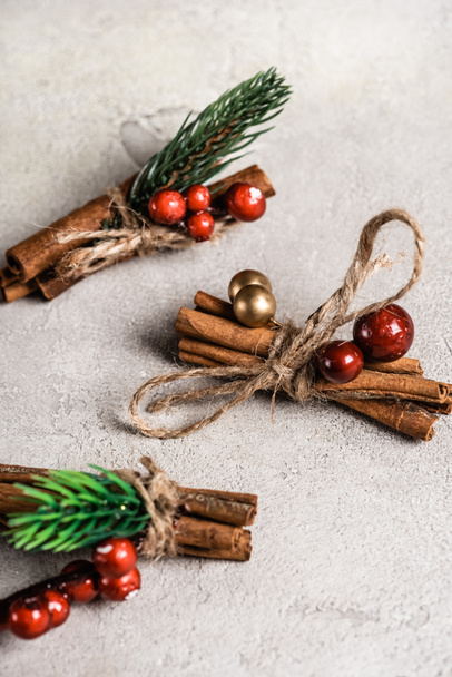 Cinnamon sticks with red beads on textured and grey background - Photo, Image