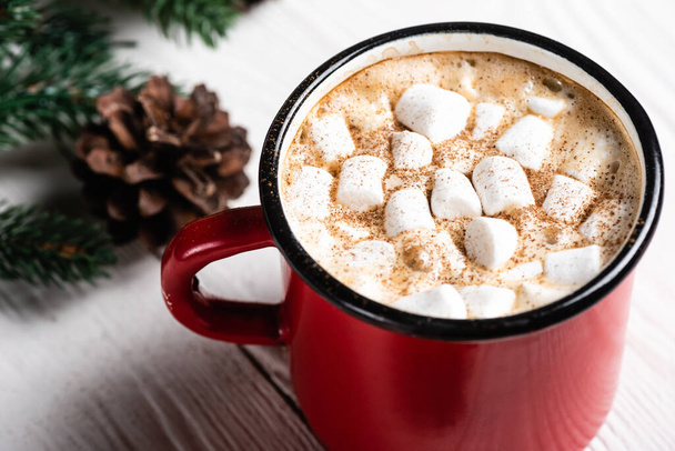Close up view of red cup of cocoa with marshmallows and cinnamon near pine cone - Фото, зображення