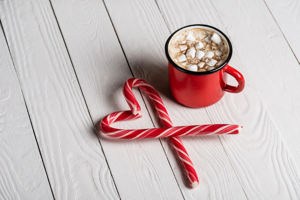 Red cup of cocoa near christmas candy canes on wooden background - Фото, изображение
