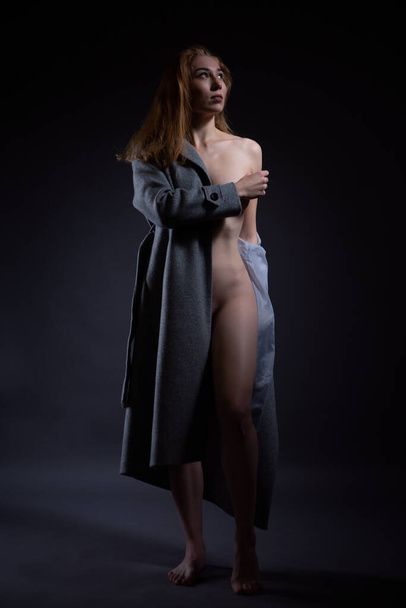 A gorgeous naked young woman in a coat slightly covers her beautiful Breasts with her hand - Photo, Image