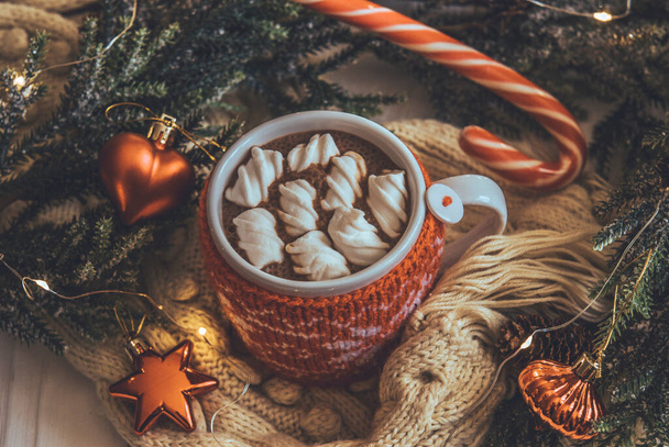 Cup of hot cocoa with marshmallows in a knitted orange case. Hot cocoa on a background of New Year's decor - Photo, image