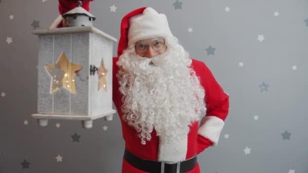 Slow motion portrait of smiling Santa holding lantern and looking at camera on glittery background - Πλάνα, βίντεο