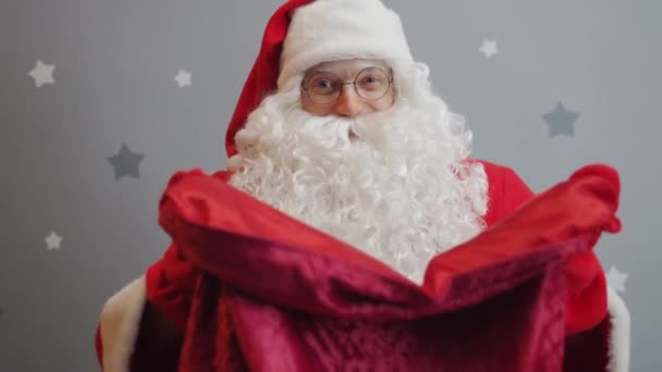 Portrait of man in Santa costume offering presents stretching arms with bag to camera - Záběry, video
