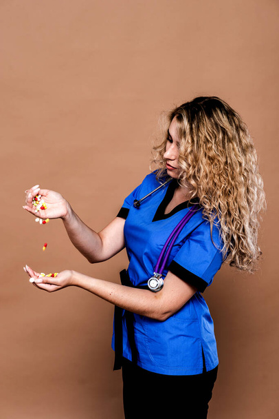 Portret młodej kobiety w garniturze medycznym ze stetoskopem na szyi, rzucającej kolorowymi tabletkami jak konfetti. Koncepcja szczęśliwego farmaceuty wolnego przed wyborem leków - Zdjęcie, obraz