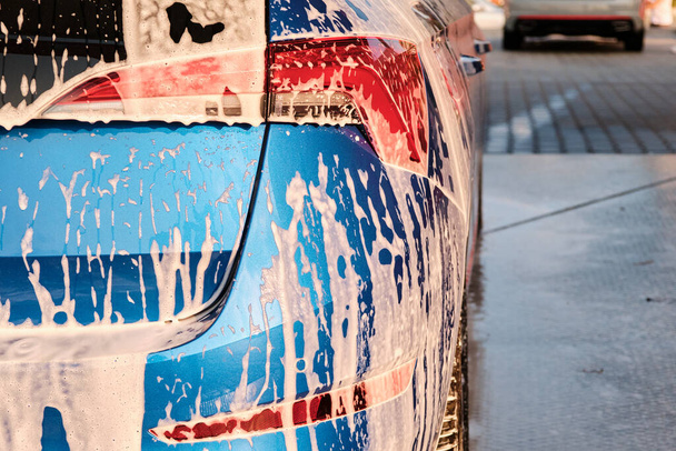 Κλείστε ένα προβολέα σε ένα σαπούνι κατά τη διάρκεια του πλυσίματος του αυτοκινήτου με αφρό. Καθαρισμός αυτοκινήτου με νερό υψηλής πίεσης. - Φωτογραφία, εικόνα