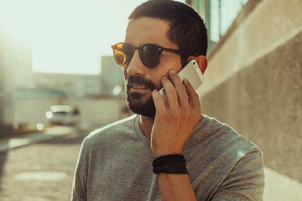 Young casual man using smartphone on the street. Wearing sunglasses, t-shirt and bracelets - Valokuva, kuva
