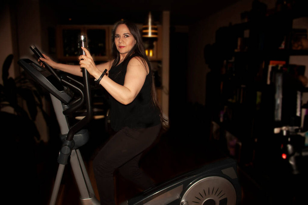 Γυναίκα άσκηση σε ένα ελλειπτικό στο σπίτι ή γυμναστήριο για τη διατήρηση της υγείας - Φωτογραφία, εικόνα