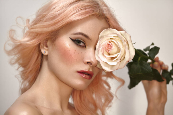 Soft-Girl Style with Trend Pink Flying Hair, Fashion Make-up. Woman Face with Fake Freckles and Rose Flower. Blonde Female Model with perfect Fresh Clean Skin, Blush Rouge. Wedding Bride Makeup - Zdjęcie, obraz