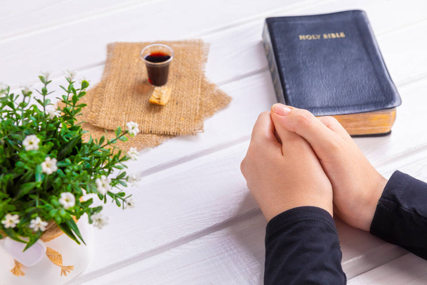 Young woman praying and Taking communion  - the wine and the bread symbols of Jesus Christ blood and body with Holy Bible. Easter Passover and Lord Supper concept Focus on her hands. - Photo, Image