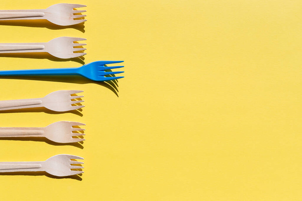 Organic bamboo disposable cutlery vs plastic ones on yellow background. Environmentally friendly wooden and non-oragnic plastic forks.ecology, zero waste concept. copyspace. - Photo, Image