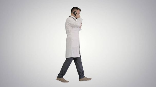 Medical doctor calling by phone walking on gradient background. - 写真・画像