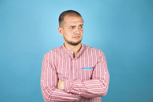 Orosz üzletember visel piros inget a kék háttér szkeptikus és ideges, rosszalló kifejezés az arcon keresztbe karok - Fotó, kép