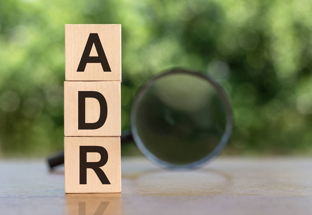 ADR Abbreviation On Wooden Blocks on table with magnifier on green background - Foto, Imagen