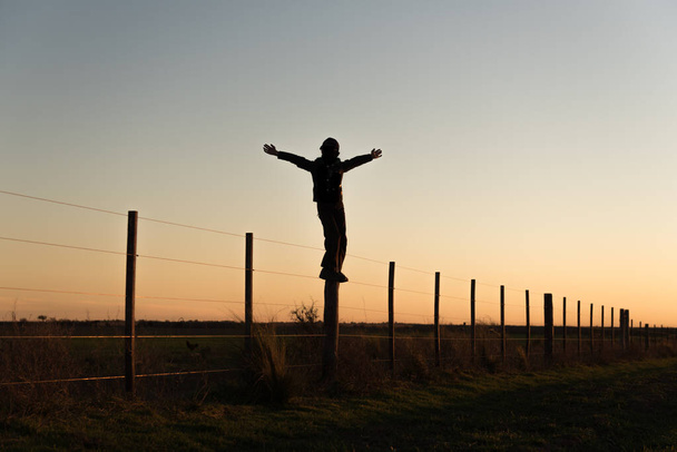 Mennoniet of amish jongen staande op een hek in een kamp gelegen aan de pampas. - Foto, afbeelding
