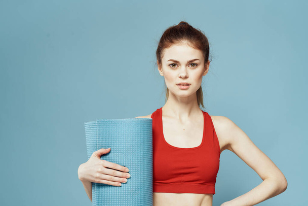 Sportovní žena tréninková podložka v ruce Red tank top cvičení modré pozadí - Fotografie, Obrázek