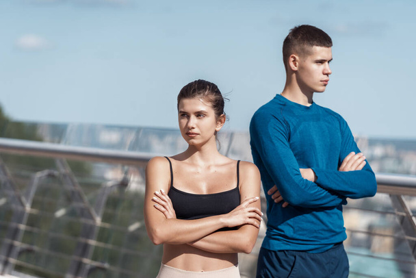 Two confident and focused young adult sporty friends looking aside, crossed hands on chest, standing outdoors after sport training together - Valokuva, kuva