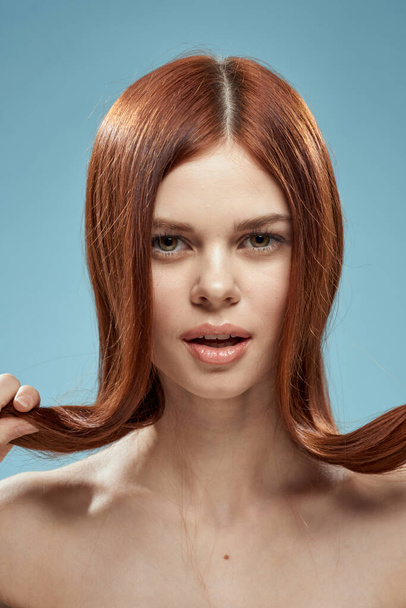 Pretty woman holding hair in hands grooming naked shoulders cropped view blue background - Foto, Imagem