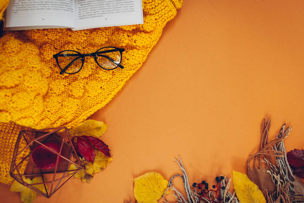 Herbstlicher Hintergrund mit Buch, Blättern, Pullover, Kerze, Schal und Gläsern. Flache Hygge-Komposition für gemütliche Herbststimmung. Weltraum - Foto, Bild