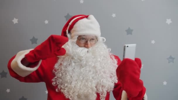 Santa Claus in headphones looking at smartphone screen and dancing having fun - Кадры, видео