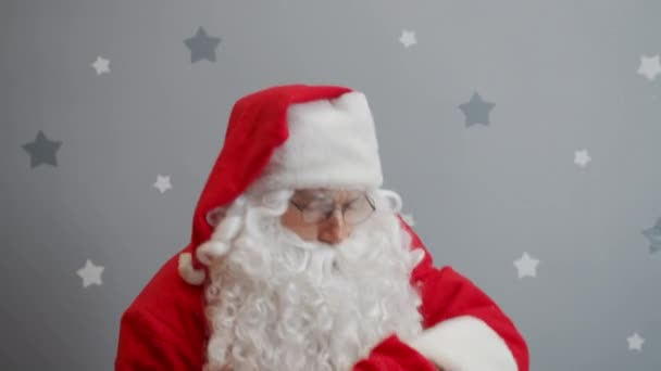 Santa raising bag of presents looking at camera and winking on starry background - Imágenes, Vídeo