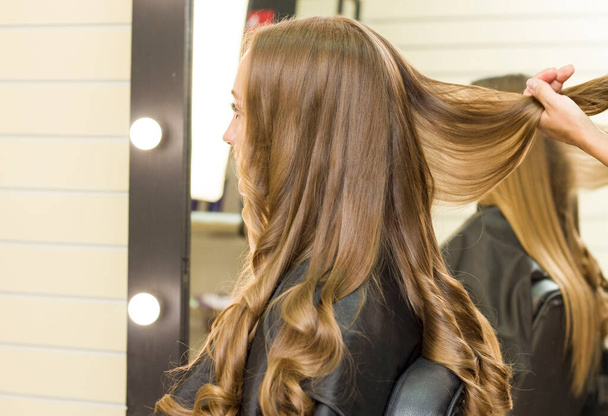 Mladá žena si nechává udělat vlasy v salónu krásy. Natahovat kudrlinky - Fotografie, Obrázek