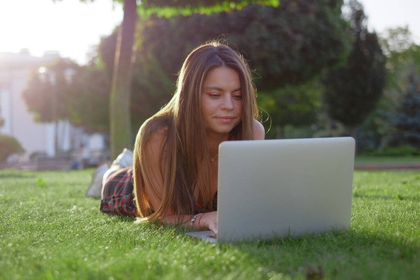 Young woman using laptop in the park lying on the green grass. Leisure time activity concept.  - Photo, Image