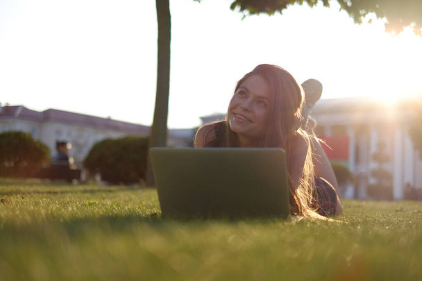 Junge Frau mit Laptop im Park auf dem grünen Rasen liegend. Freizeitkonzept.  - Foto, Bild