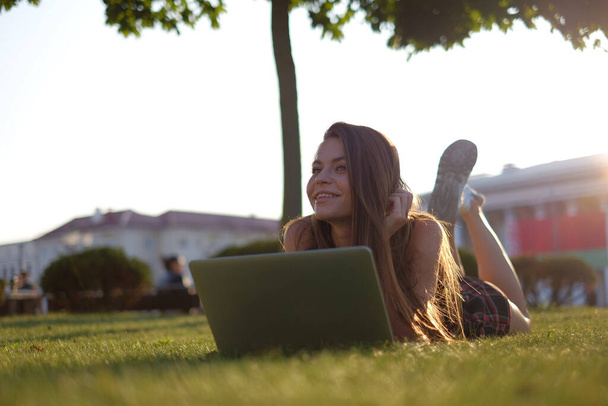Young woman using laptop in the park lying on the green grass. Leisure time activity concept.  - Foto, Bild