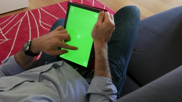 El hombre mira la tableta acostada en el sofá y desplaza las páginas de abajo hacia arriba, tableta con pantalla de cromo - Metraje, vídeo