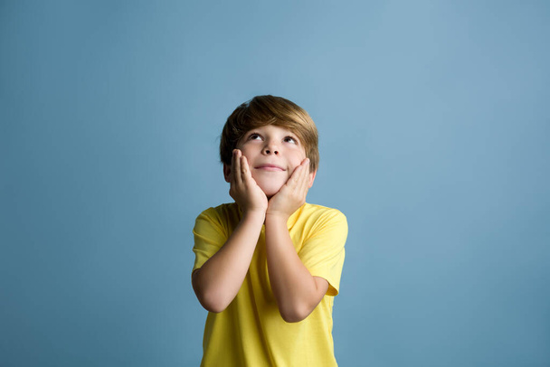 Smiling beautiful child thinking and looking upward. Portrait of child on colored blue background - Photo, Image