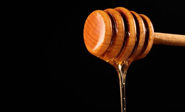 Miel dégoulinant de trempette au miel en bois sur fond noir. - Photo, image