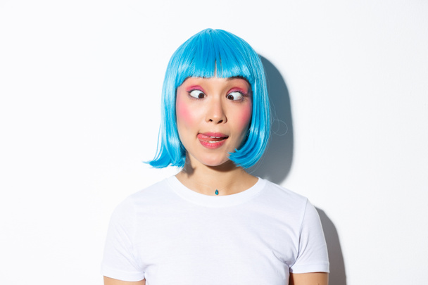 Közelkép vicces és buta ázsiai lány szórakoztató ünneplő halloween, visel kék paróka és hunyorgó, feltűnő grimaszok - Fotó, kép