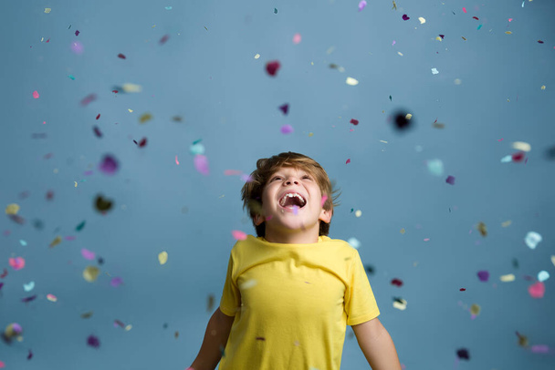 Sonriendo hermosa niña saltando en confeti. Retrato de niño sobre fondo azul. - Foto, imagen