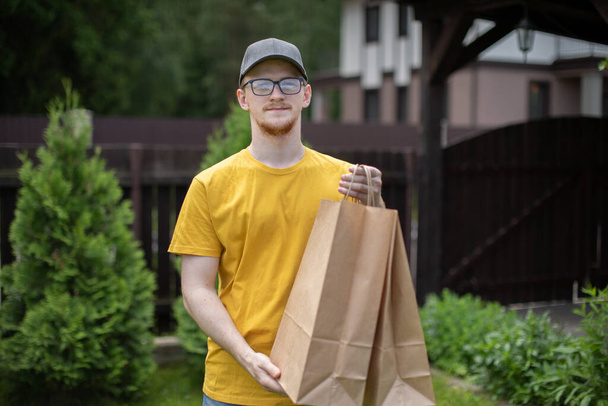Smart delivery man in yellow t-shirt carrying biodegradable paper bags outdoors - Photo, Image