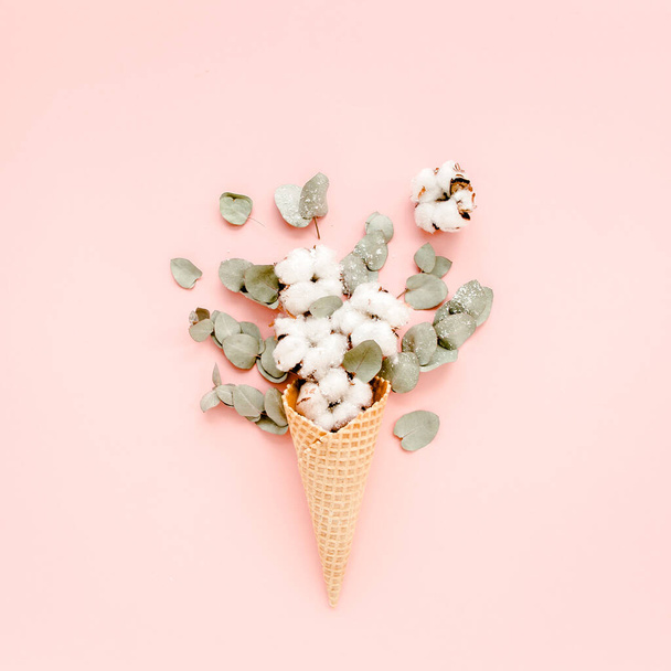 Waffle cone with cotton bouquet and eucalyptus leaves on pink background, flat lay, top view - Zdjęcie, obraz