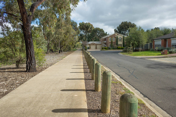 遠くにいくつかの郊外の家と静かな住宅街の歩行者通路。ユーカリの木が長い道路を持つオーストラリアの郊外のコンクリートの歩道。テキストのコピースペース. - 写真・画像