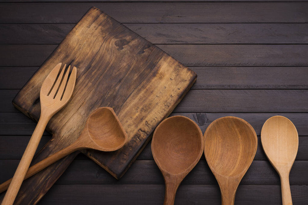 Kuchyňské potřeby řezací deska Dřevěná lžíce a vidlička na staré černé dřevěné podlahy horní pohled - Fotografie, Obrázek
