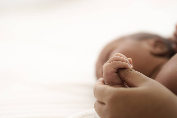 Αφροαμερικανό βρέφος ξαπλωμένο στο κρεβάτι ενώ τα χέρια της μητέρας σηκώνουν το μωρό. - Φωτογραφία, εικόνα