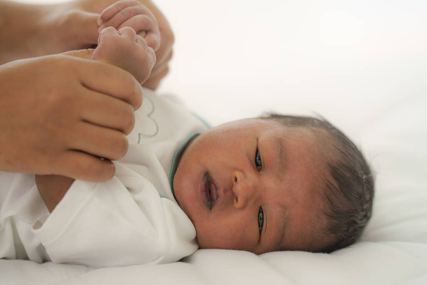 Αφροαμερικανό νεογέννητο μωρό ξαπλωμένο στο κρεβάτι με το χέρι της μητέρας να κρατάει και τα δύο χέρια - Φωτογραφία, εικόνα