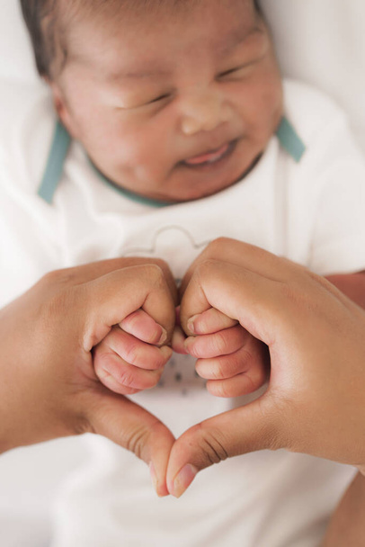 μητέρα χέρια κάνοντας σχήμα καρδιάς, ενώ κρατώντας το μωρό χέρια - Φωτογραφία, εικόνα