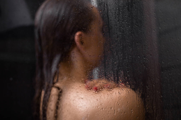 mujer joven desnuda cogida de la mano en el hombro teniendo cuidado de la piel en el fondo negro - Foto, imagen