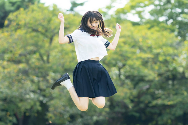 Ασιάτισσα μαθήτρια λυκείου που χοροπηδάει με χαμόγελο στο πάρκο - Φωτογραφία, εικόνα
