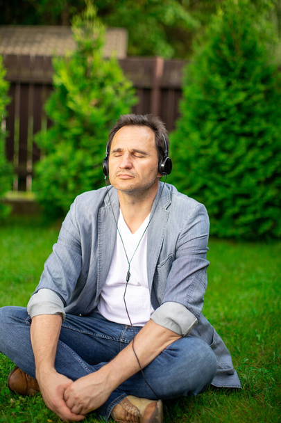 Στρεσαρισμένος άνθρωπος σε ακουστικά ψύξη σε εξωτερικούς χώρους ακούγοντας μουσική με κλειστά μάτια - Φωτογραφία, εικόνα