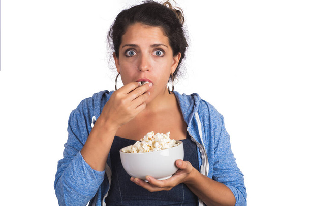 Muotokuva nuoresta naisesta, joka näyttää pelokkaalta katsoessaan elokuvaa ja syödessään popcornia studiolla. Eristetty valkoinen tausta. - Valokuva, kuva